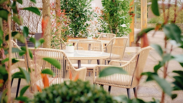 A round table with wicker chairs in an outdoor setting, surrounded by greenery and a pergola structure. - Wilding Hotel (Kirkby Stephen)