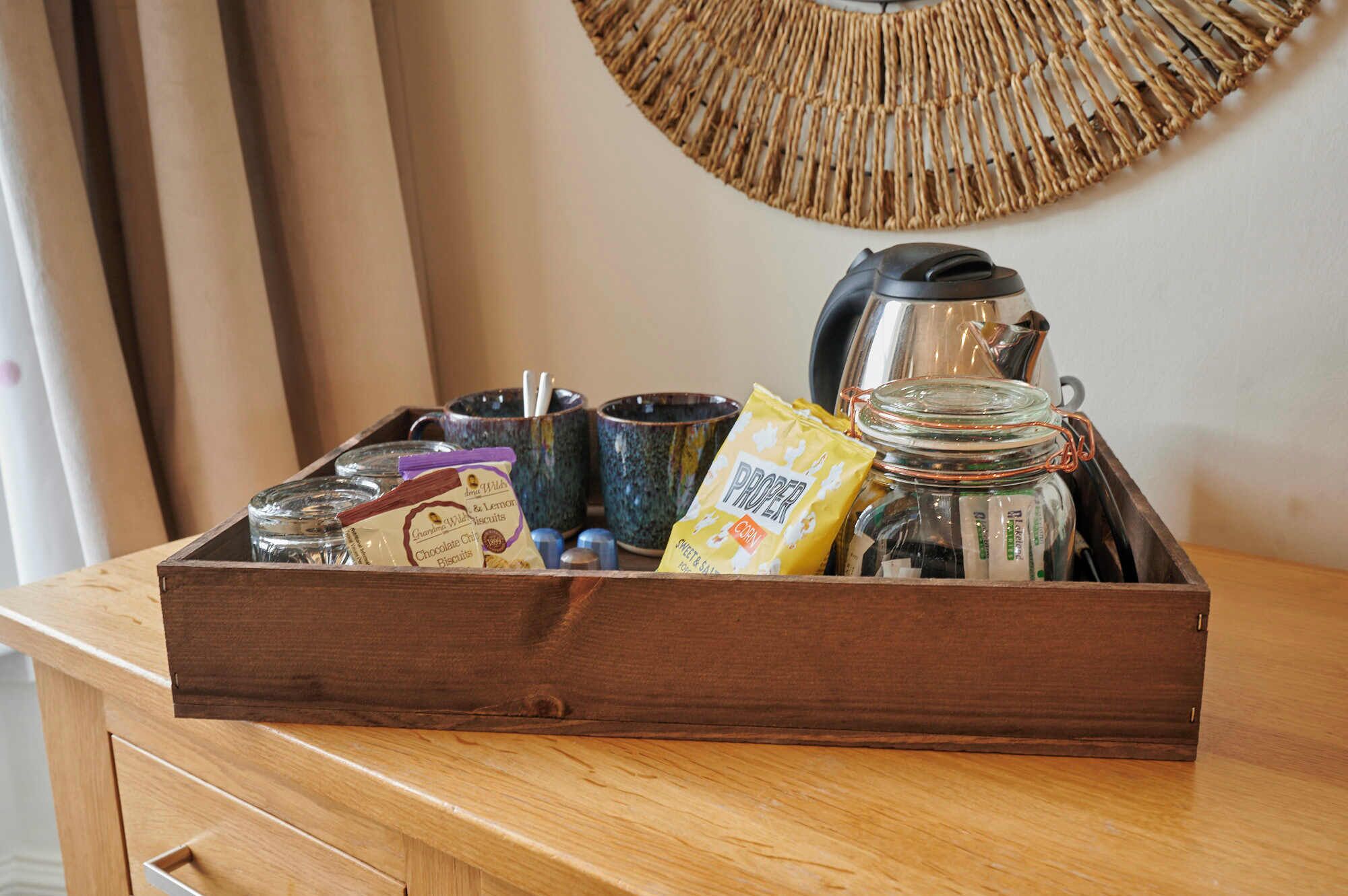 Una bandeja de madera con un juego de té, una taza, un paquete de galletas y un frasco de vidrio sobre una mesa de madera.