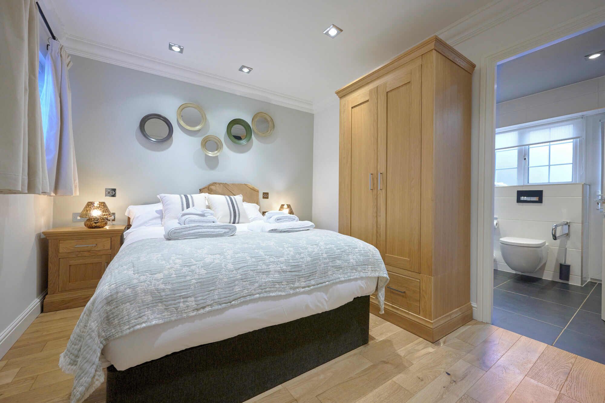 Un dormitorio con cama, mesitas de noche, armario y baño a la vista a través de una puerta abierta.