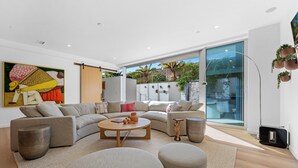 A modern living room with a sectional sofa, a round coffee table, and a large window offering a view of greenery outside.
