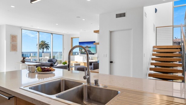 A modern kitchen with a double sink, large windows, and a view of the ocean.