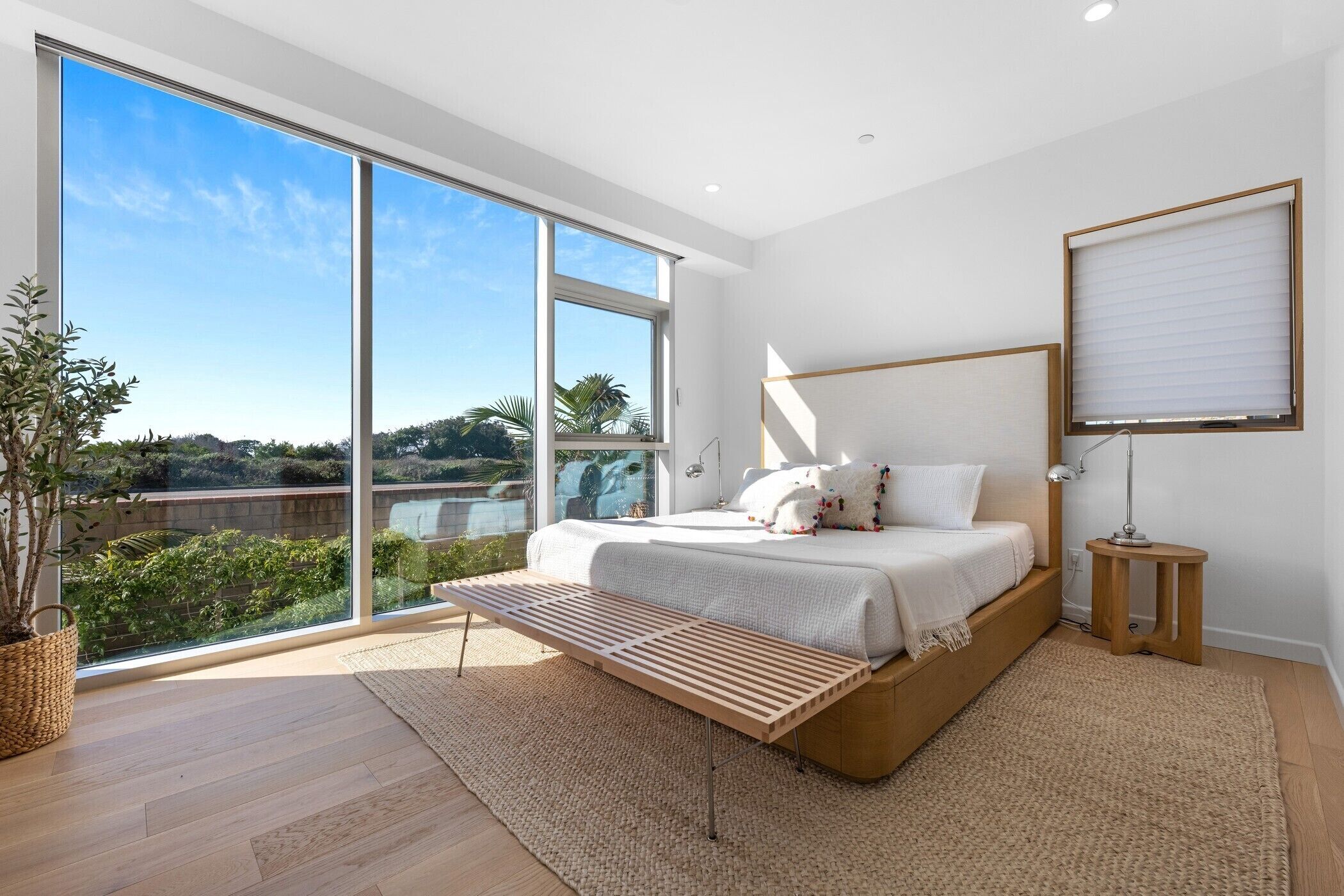 A modern bedroom with a large bed, a view of the outdoors, and a wooden bench.