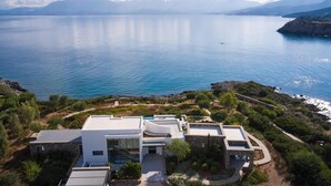 Une villa moderne dotée d’une piscine, entourée d’une végétation luxuriante et offrant une vue sur une mer calme.