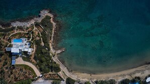 Vue aérienne d’une propriété située sur la côte, avec une piscine, plusieurs bâtiments et une plage.