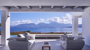 Un espace extérieur moderne, aménagé avec des meubles en osier et offrant une vue sur la mer et les montagnes.
