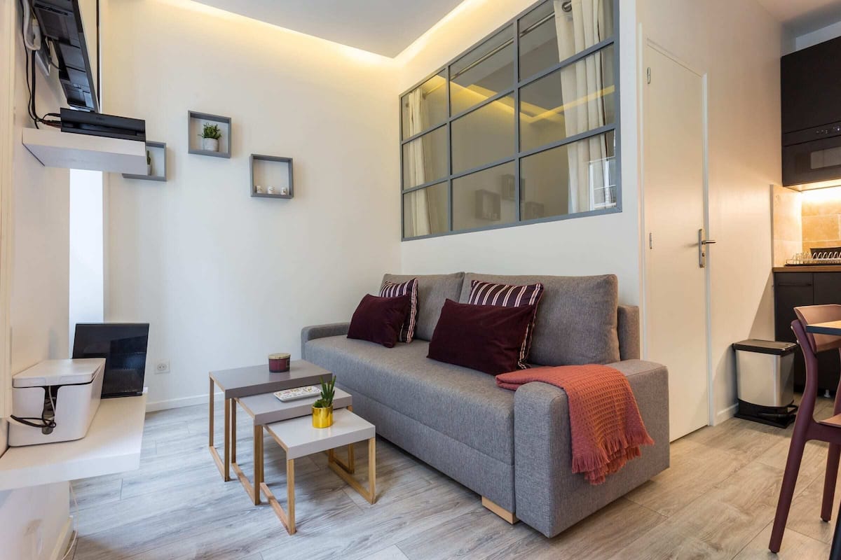 A modern living room with a grey sofa, a small table, a TV, and a window with curtains.