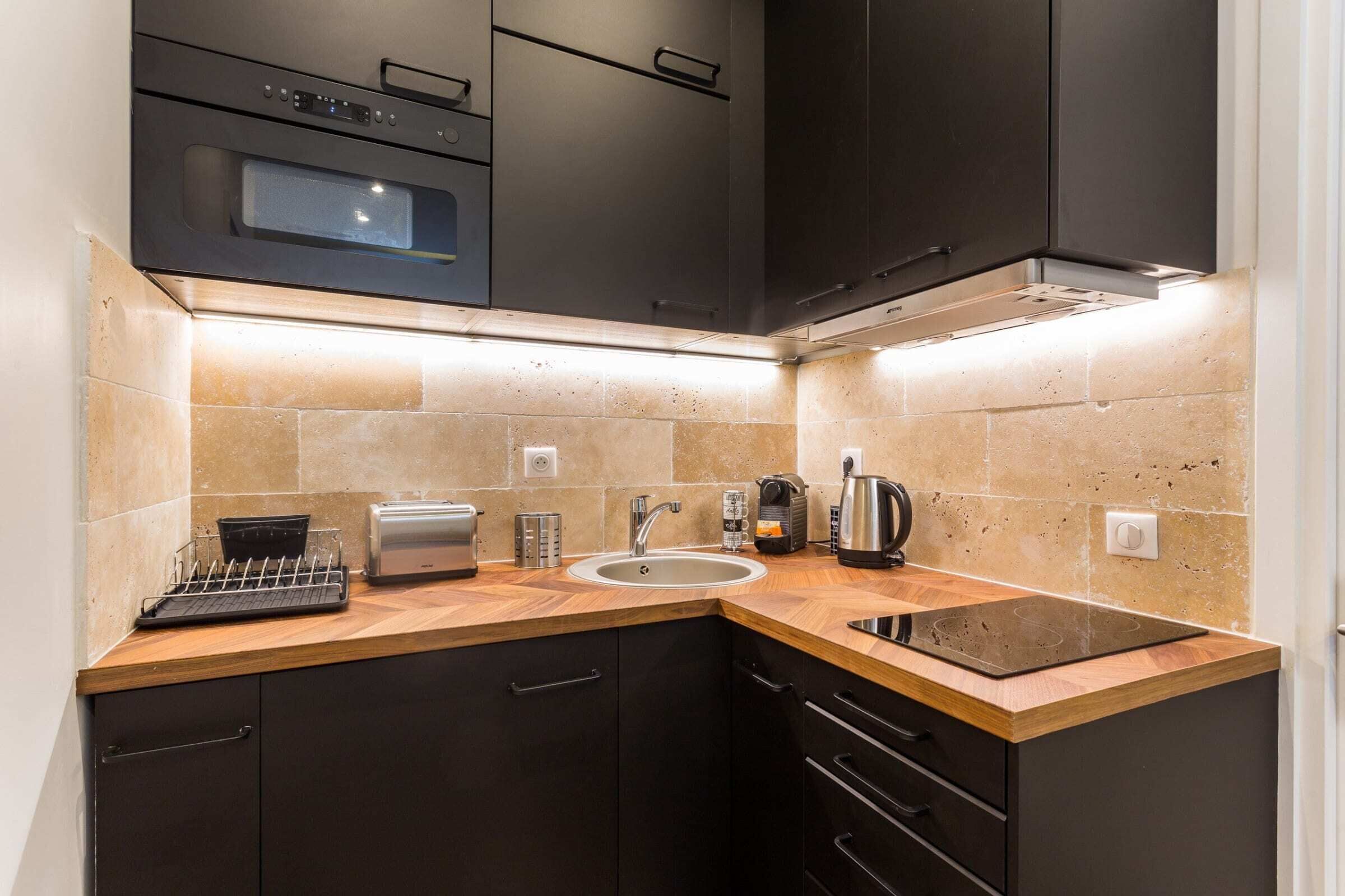 A modern kitchen with dark cabinets, a built-in oven, a sink, and a countertop with a kettle and toaster.