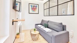 A modern living room with a grey sofa, a mounted TV, a framed tiger artwork, and a large window.