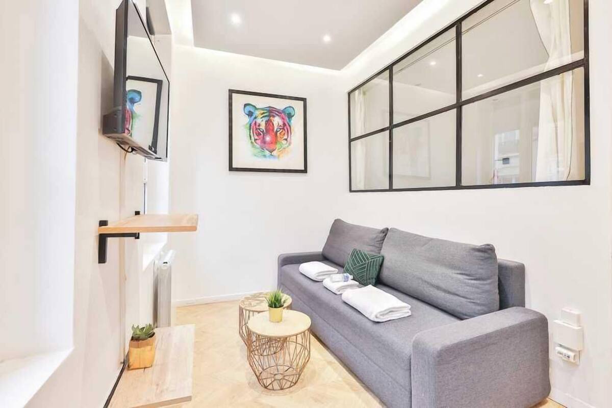 A modern living room with a grey sofa, a mounted TV, a framed tiger artwork, and a large window.