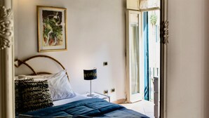 A bedroom with a bed, a nightstand, a lamp, a framed picture on the wall, and a large mirror. - Estate4home - Trevi Fountain Apartment (Rome)