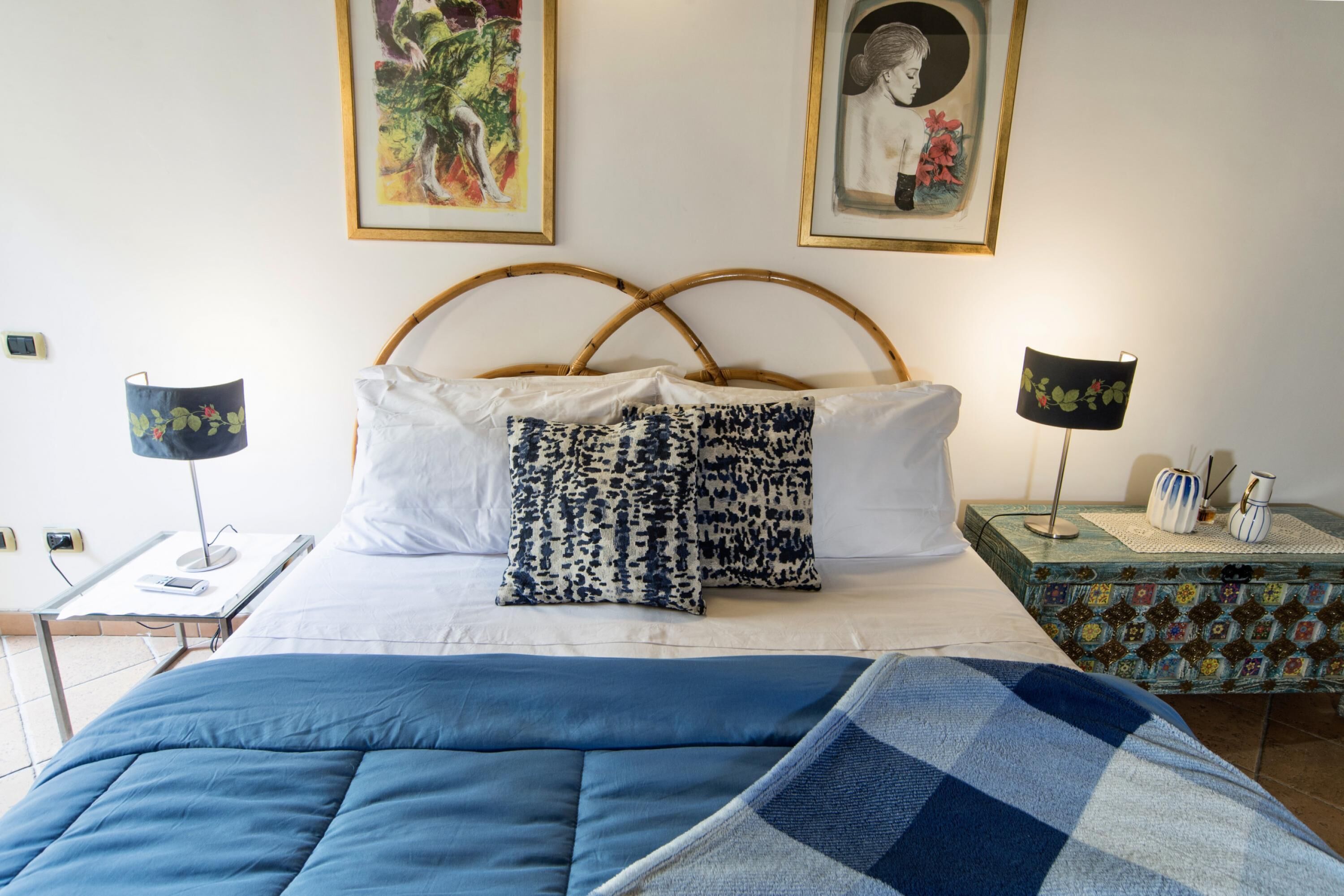 A neatly made bed with a blue blanket, two bedside lamps, and a decorative nightstand with a patterned box.