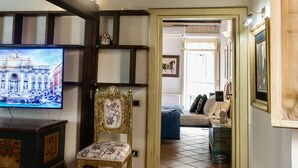 A room with a wooden ceiling, a television, a chair, a patterned rug, and a bed with pillows. - Estate4home - Trevi Fountain Apartment (Rome)