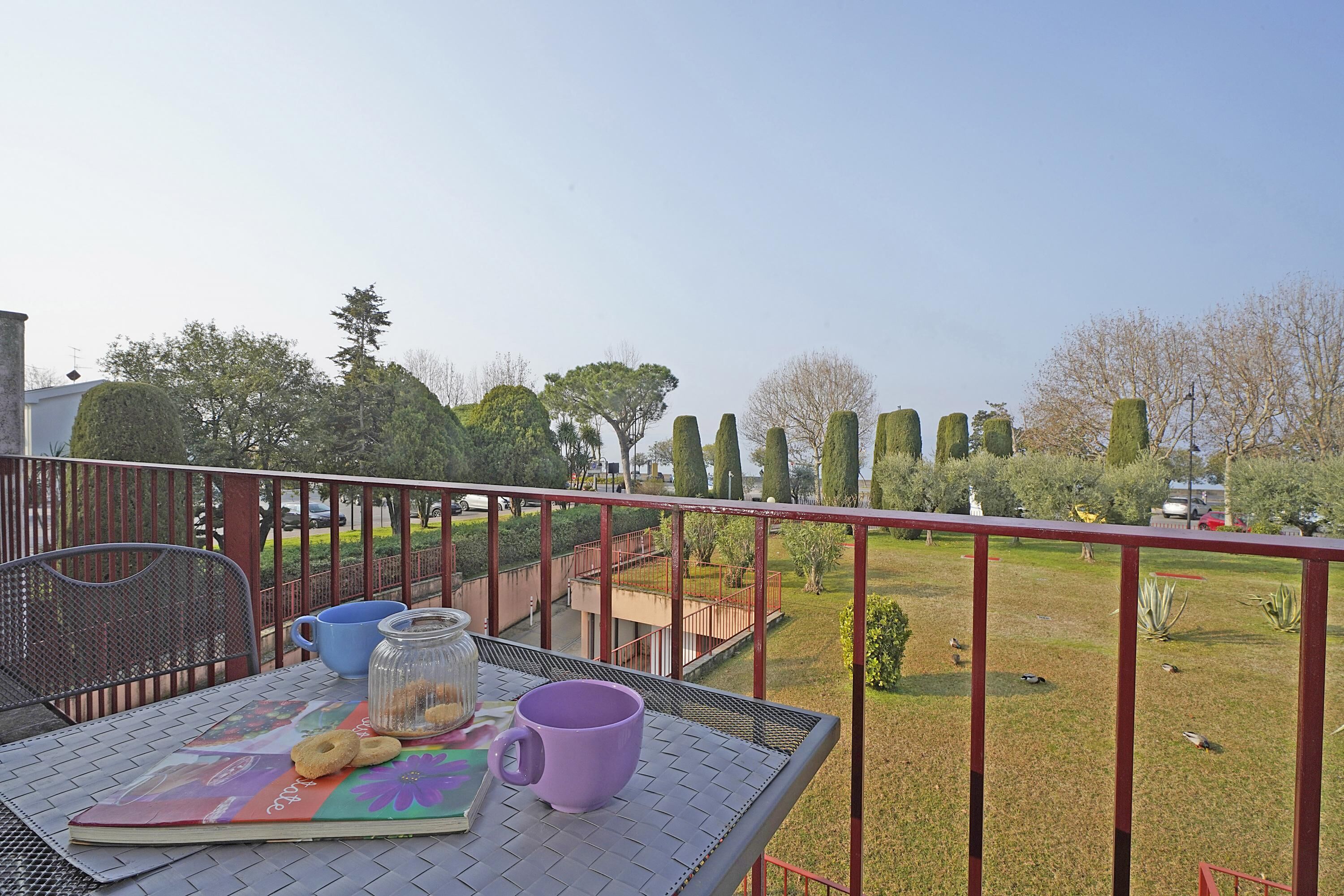 Un balcon avec une table dressée pour un repas, une vue sur un jardin bien entretenu et un ciel dégagé.
