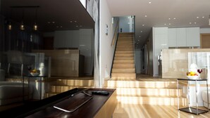 A modern kitchen with a wooden staircase, a dining area with a long table, and a kitchen island with a fruit bowl and wine glass. - Villa Magnolia Zadarvillas (Zadar)