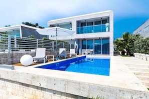 A modern poolside area with a rectangular pool, white lounge chairs, and a large umbrella. - Villa Magnolia Zadarvillas (Zadar)