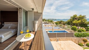 A balcony with a bed, a table with a fruit bowl and drinks, and a view of a pool and landscape. - Villa Magnolia Zadarvillas (Zadar)