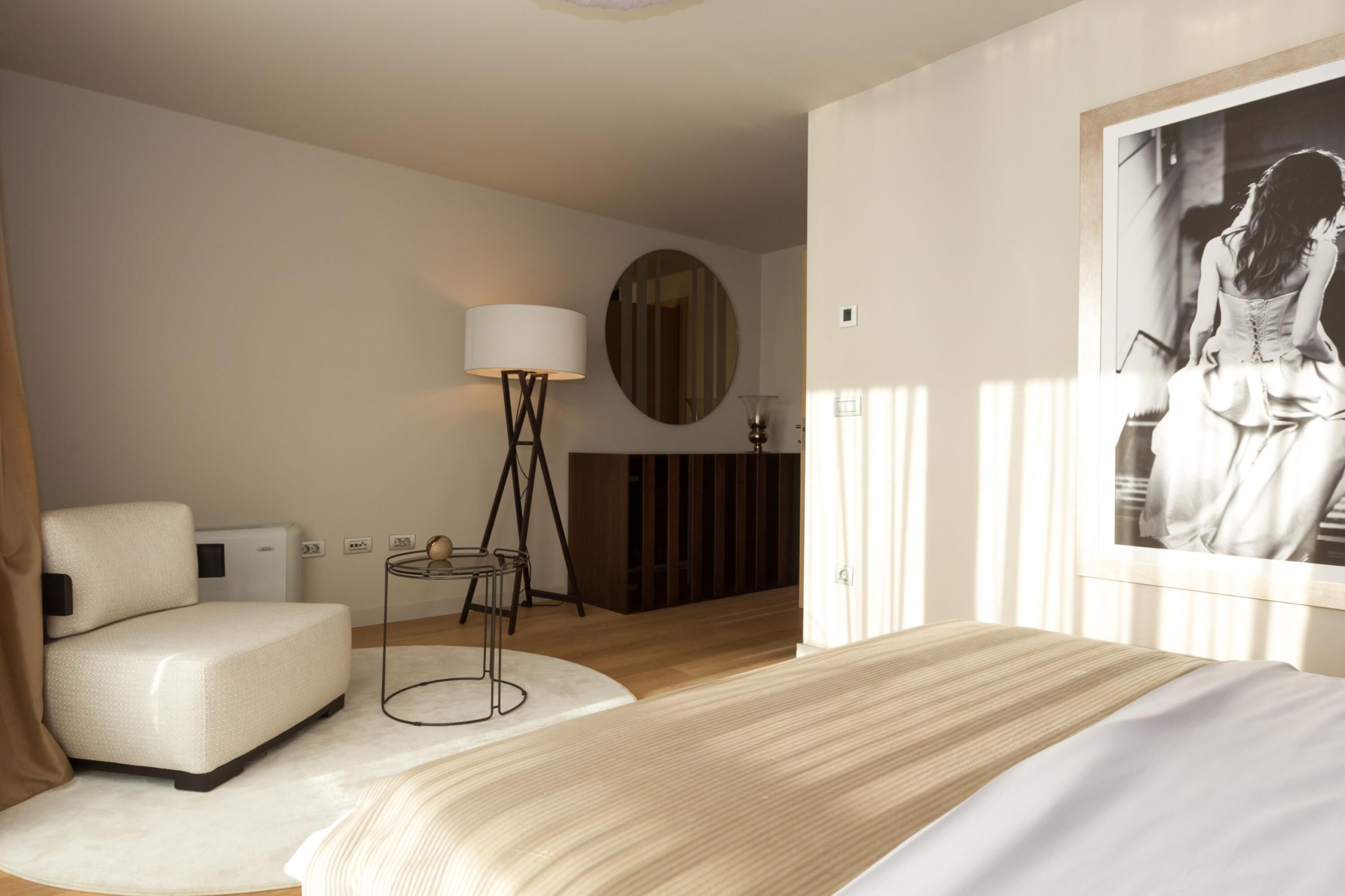 A modern hotel room with a large bed, a sofa, a standing lamp, a mirror, and a large framed picture on the wall.