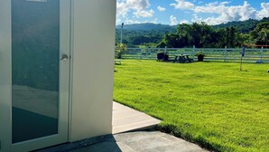 Vista de un área verde con un edificio blanco, un letrero que indica baños y una cerca blanca.