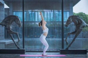 A person performing yoga on a pink mat in front of a glass wall with horse sculptures.