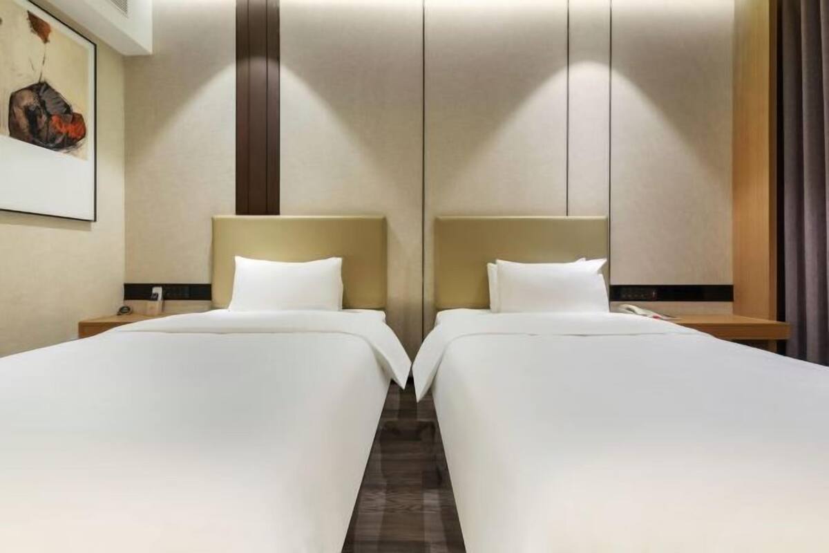 Een hotelkamer met twee bedden, een houten nachtkastje met een telefoon en een aan de muur hangend kunstwerk.