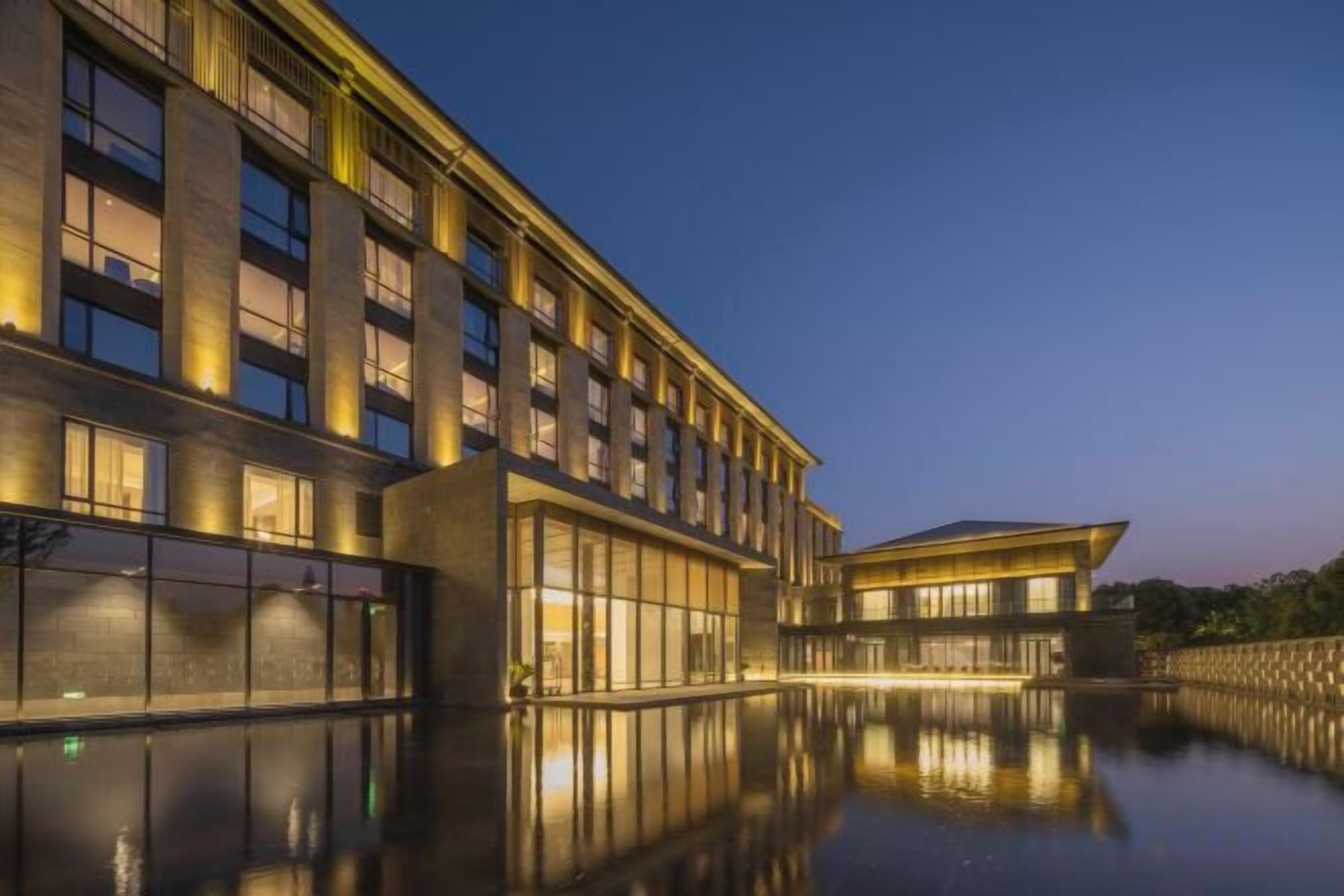A modern hotel with a reflective pool in front, large windows, and a well-lit facade.