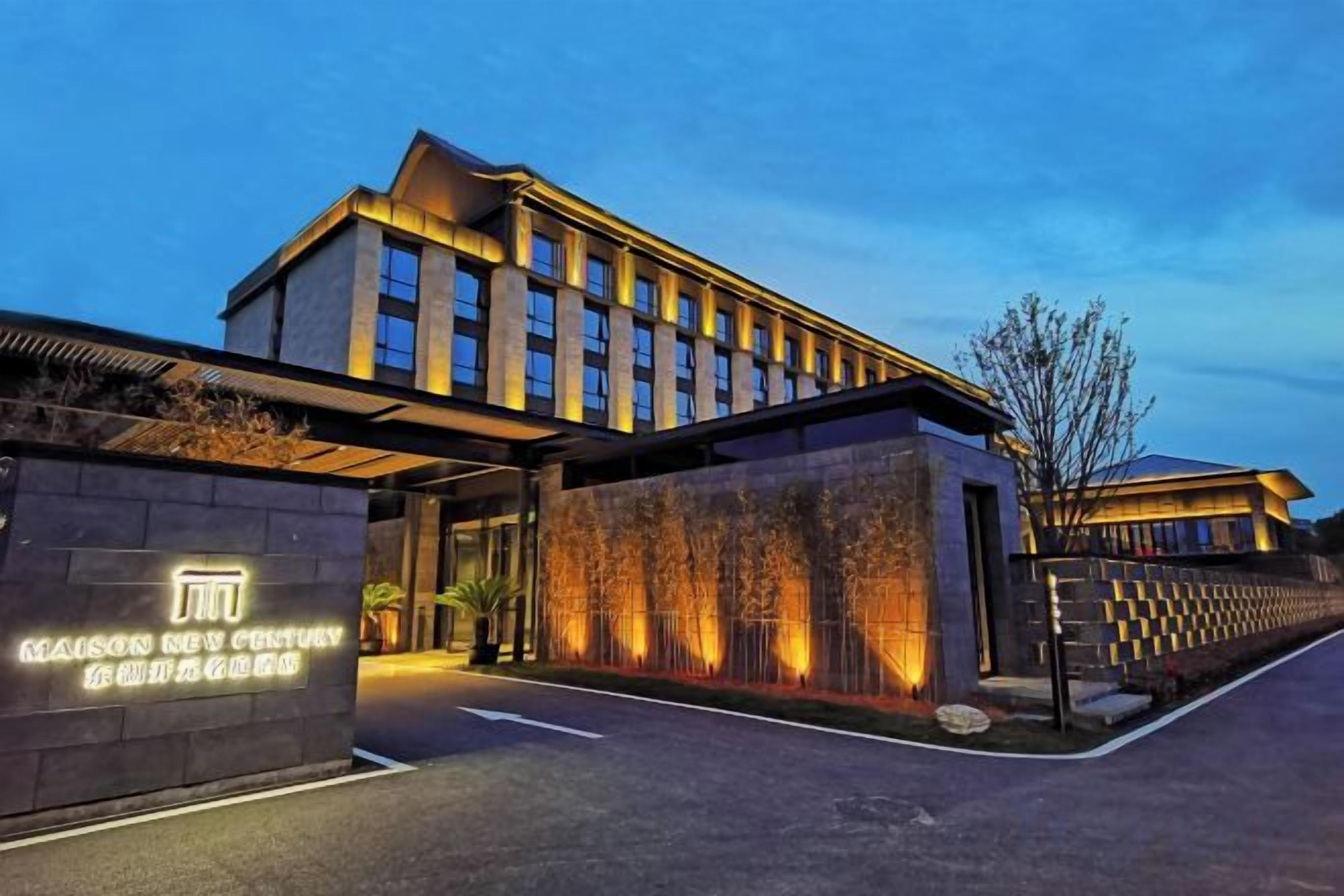 Un hotel moderno con una entrada amplia, una fachada bien iluminada y una zona ajardinada con árboles.