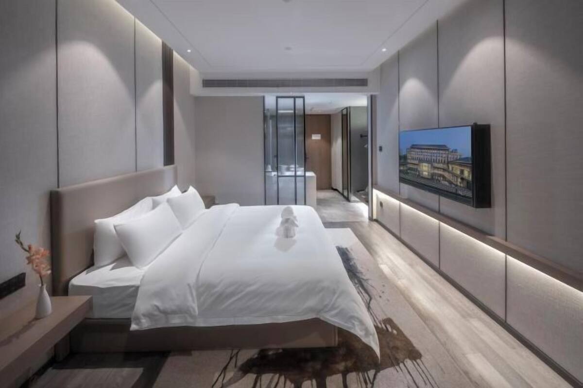 Een moderne hotelkamer met een groot bed, een flatscreen-televisie aan de muur en een glazen scheiding tussen de kamer en de gang.
