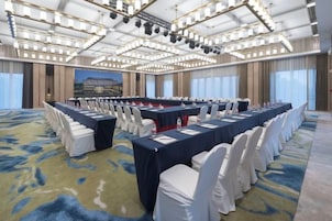 Un salón de conferencias con una larga mesa, sillas blancas y suelo alfombrado.