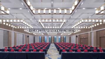 A large conference room with rows of tables and chairs, a high ceiling with modern lighting fixtures, and a carpeted floor.