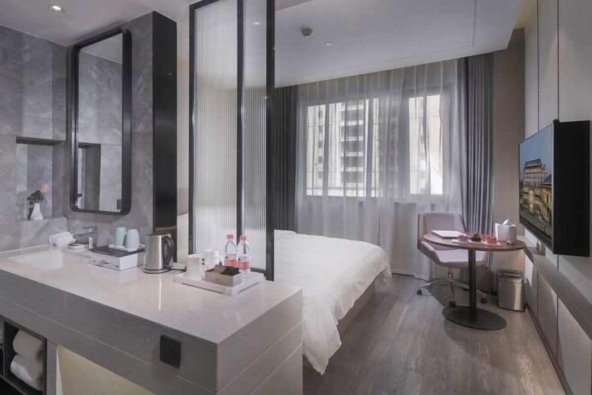 Una habitación de hotel moderna con una cama grande, un escritorio con una silla, un baño con espejo y un televisor en la pared.