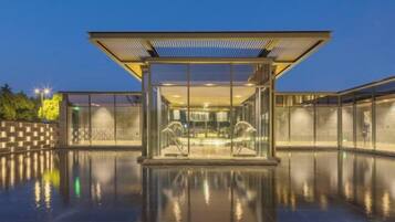 A modern building with a glass facade, a reflective pool, and a covered seating area.