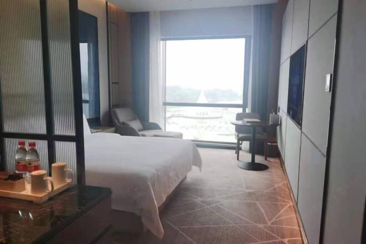 Hotelkamer met een bed, bureau met ontbijtartikelen, een stoel, een klein tafeltje en een groot raam met uitzicht.