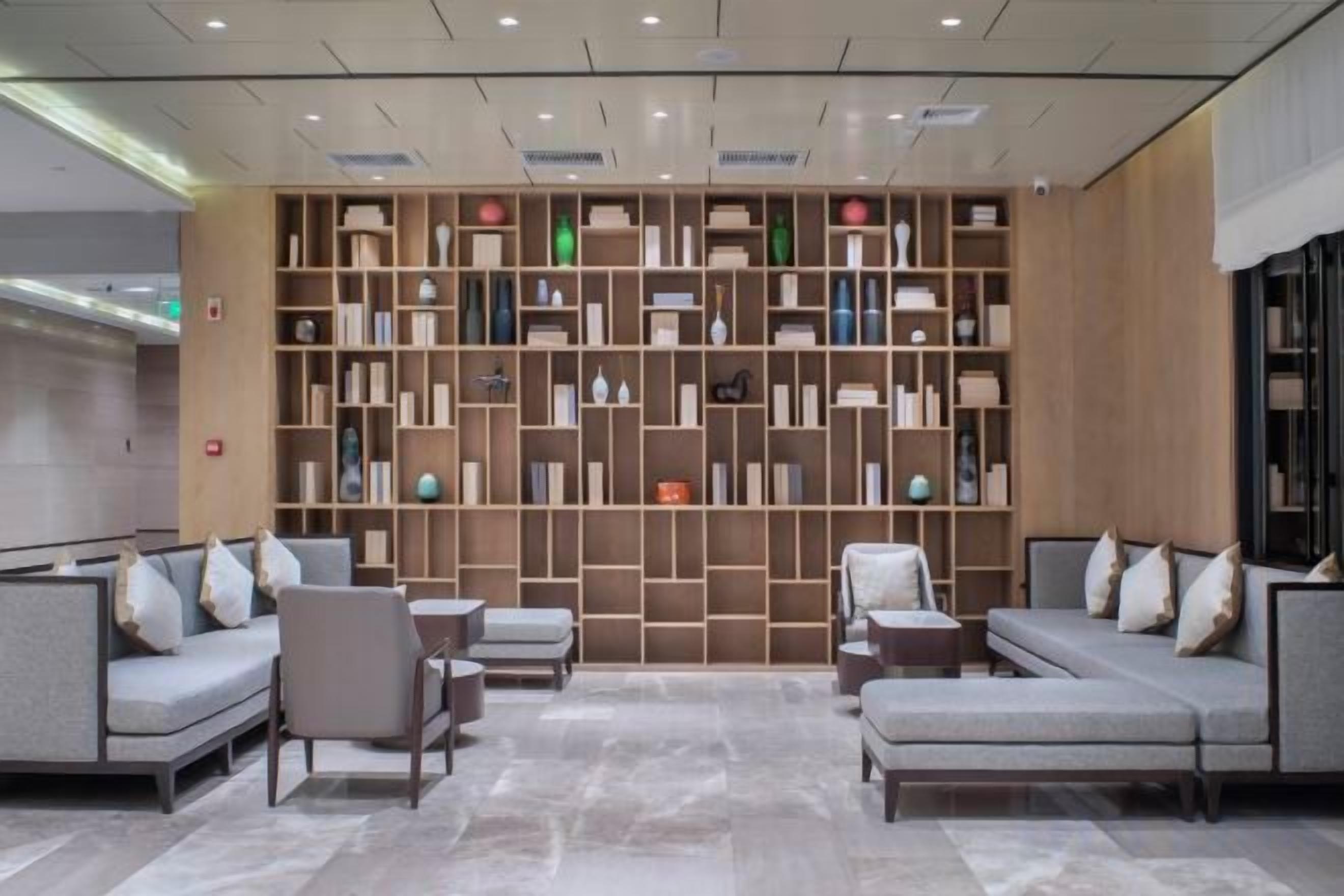 A modern lobby with a seating area, a bookshelf wall, and a reception desk.