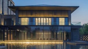 A modern building with a glass facade, a pool area with seating, and a well-lit entrance. - Wuhu Maison New Century Hotel (Wuhu)