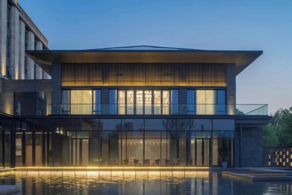 Un edificio moderno con fachada de vidrio, un área de piscina con asientos y una entrada bien iluminada.