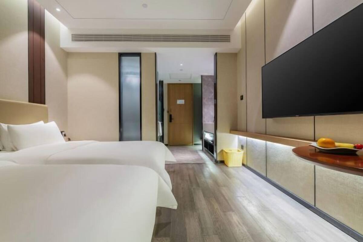 Een hotelkamer met twee bedden, een wandgemonteerde flatscreen-tv en een klein tafeltje met fruit.