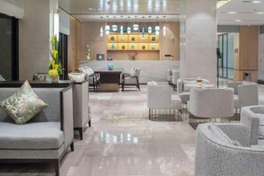 Een hotellobby met zithoeken, een receptiebalie en een decoratieve muur met verlichting.
