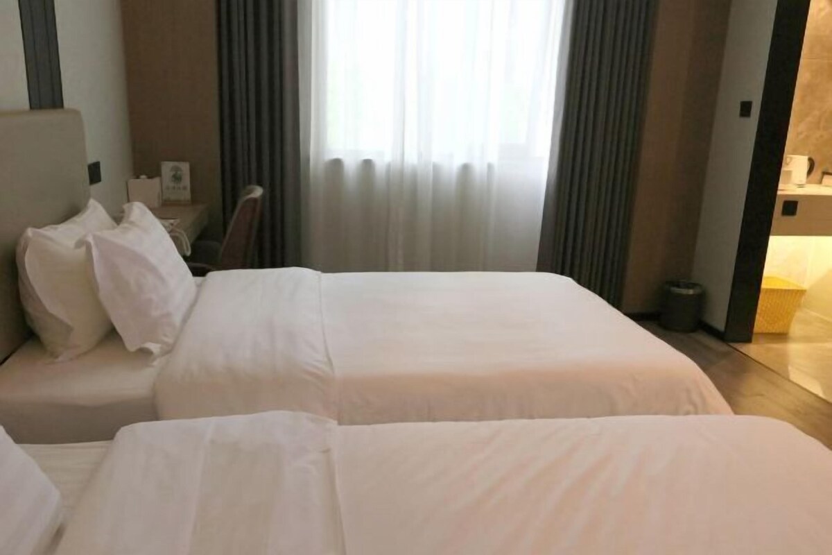 Habitación de hotel con dos camas, una mesita de noche, una silla y una ventana con cortinas.