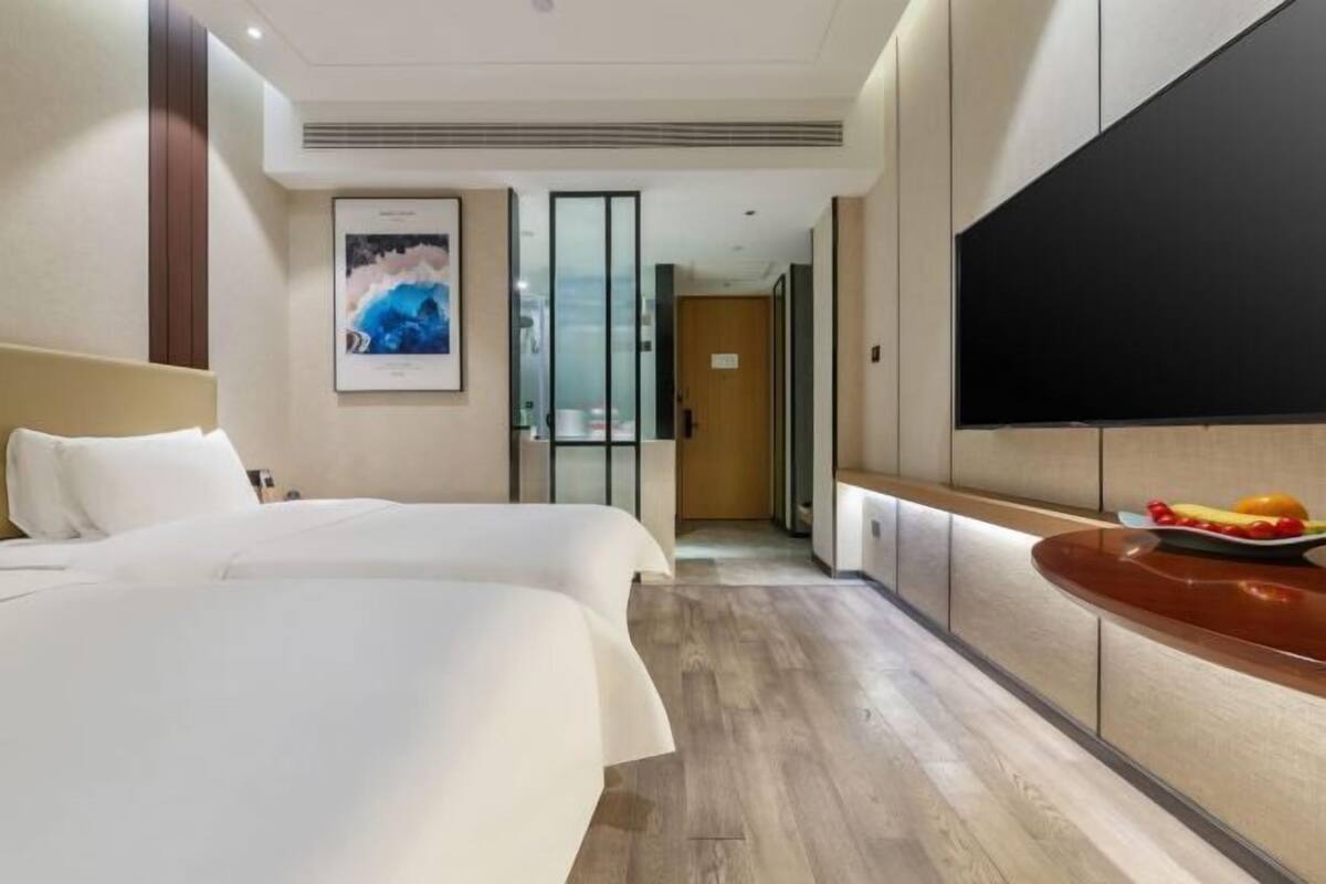 Een hotelkamer met twee bedden, een flatscreen-tv, een houten vloer en een ingelijst schilderij aan de muur.