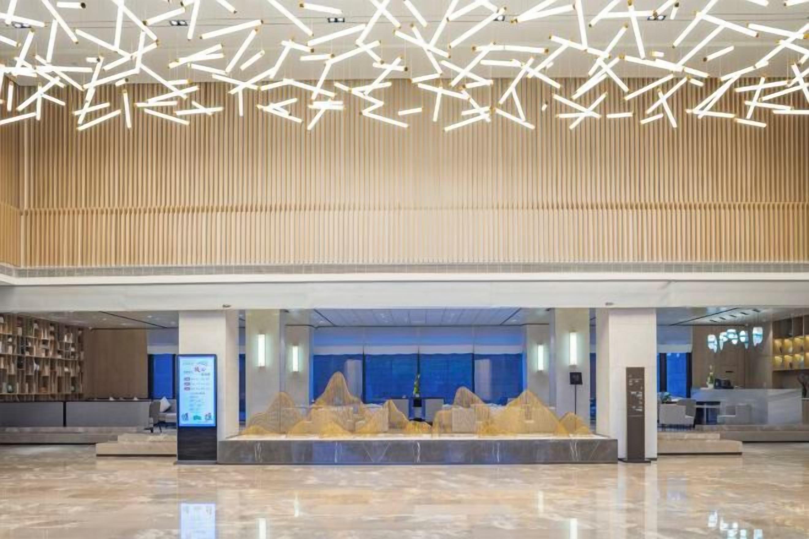 Un hall d’entrée spacieux, doté d’un plafond au design moderne, d’un comptoir de réception et d’un espace salon offrant une vue sur l’intérieur.