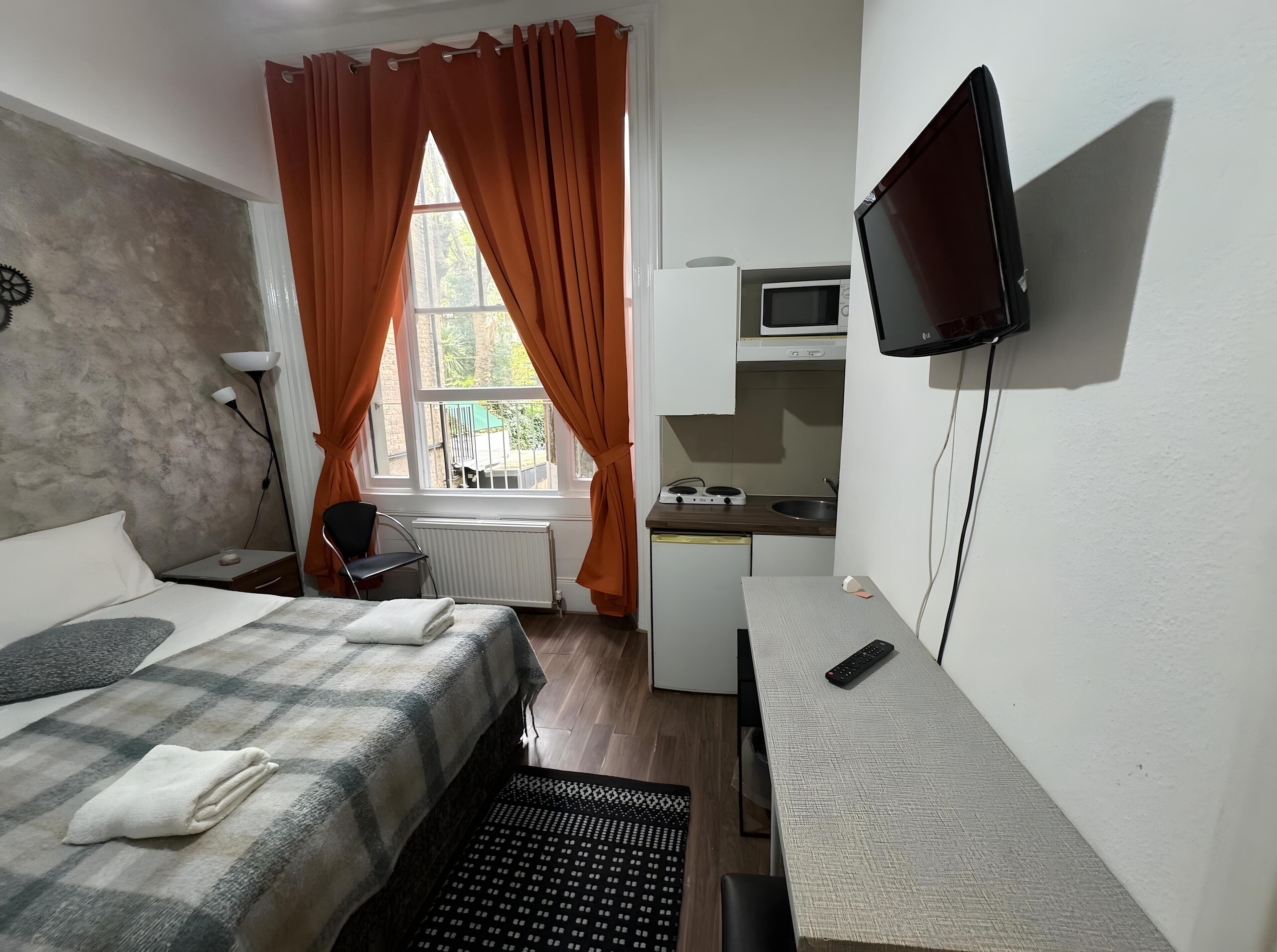 A compact hotel room with a bed, a desk, a TV, and a kitchenette.