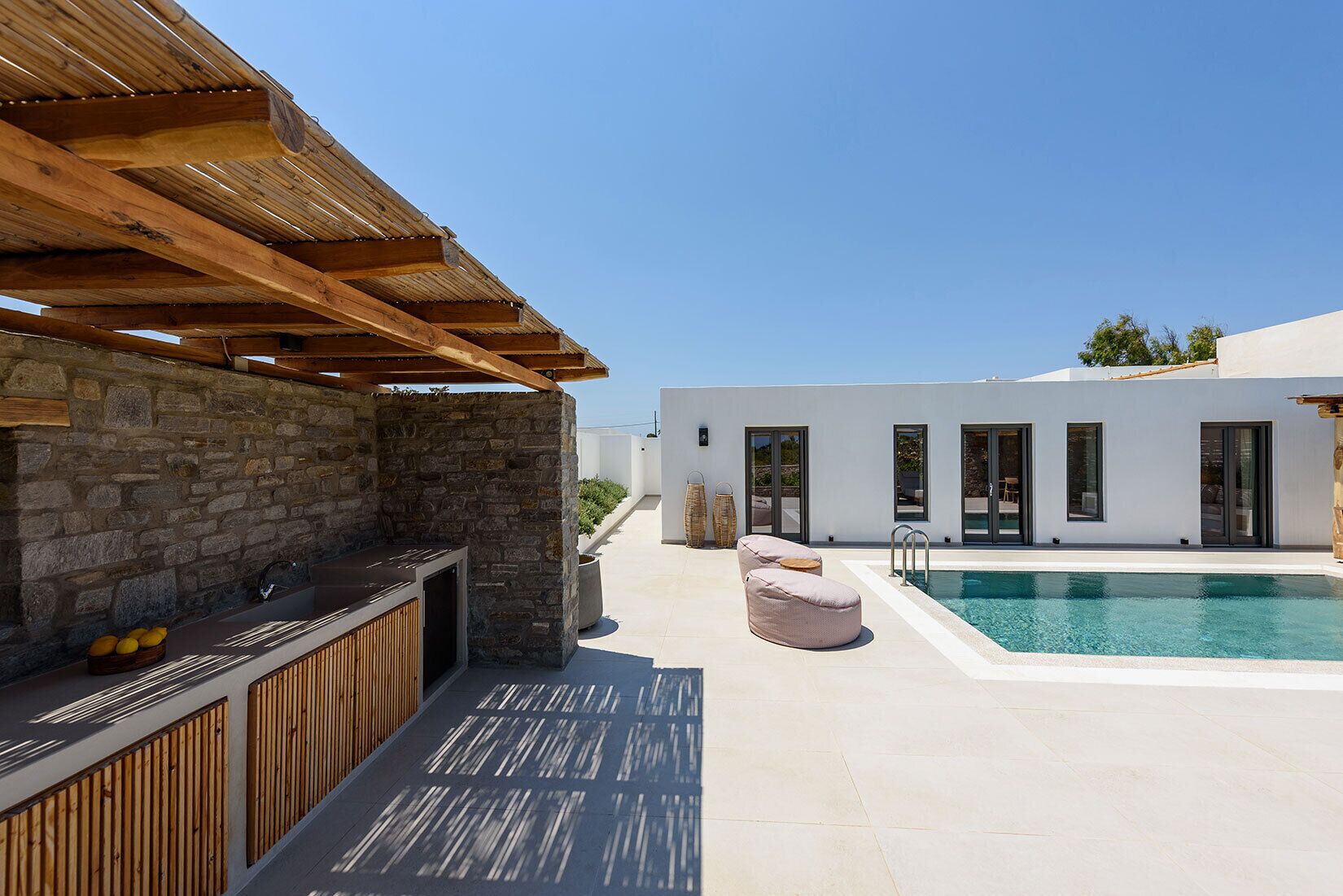 A modern outdoor area with a stone fireplace, a pool, and a covered seating area.