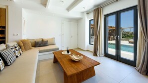 Ein modernes Wohnzimmer mit einer Couch, einem Couchtisch und Blick auf einen Swimmingpool durch große Schiebeglastüren.
