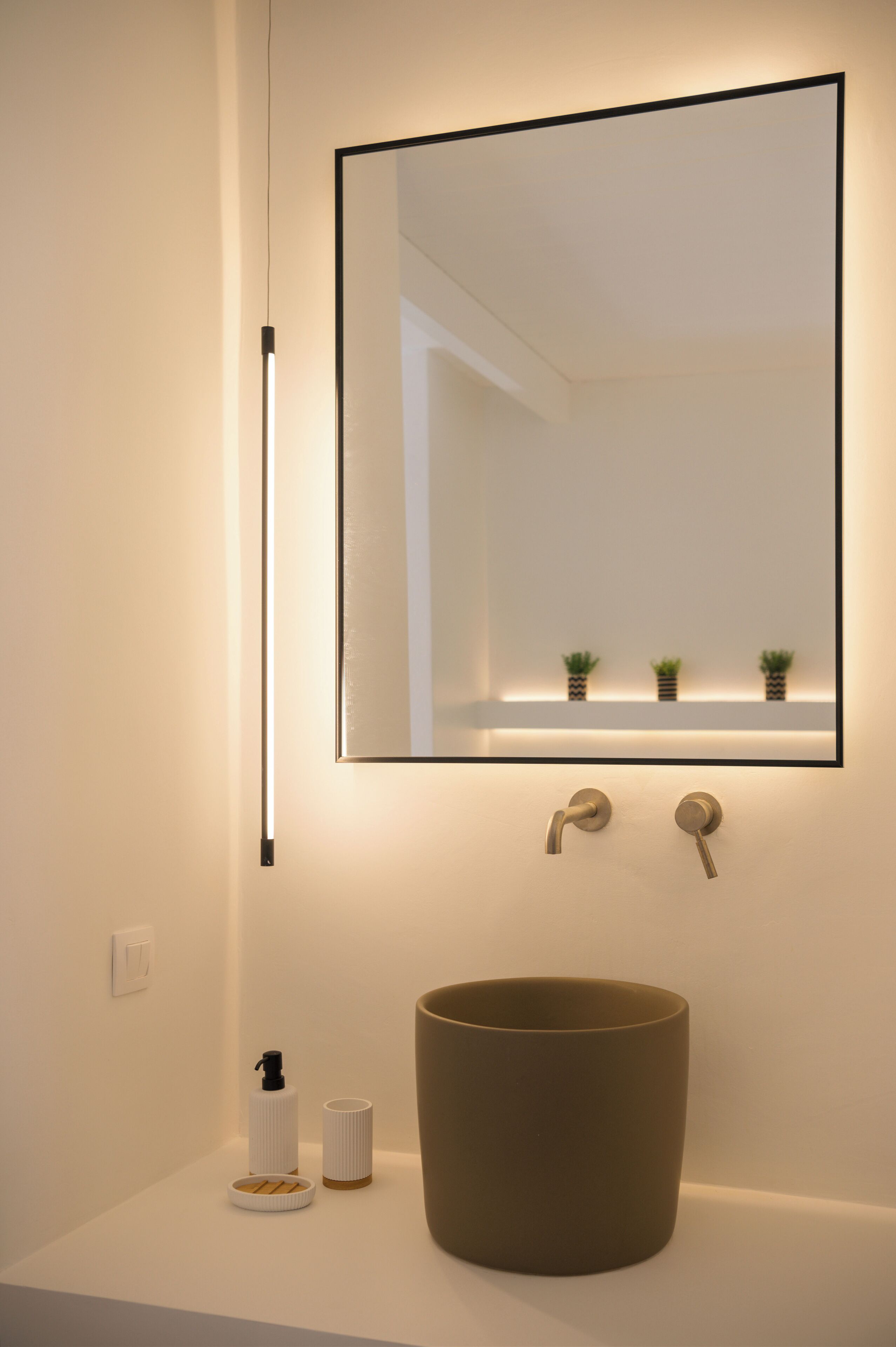 Un bagno con uno specchio grande, un lavandino tondo e un piccolo ripiano con piante.