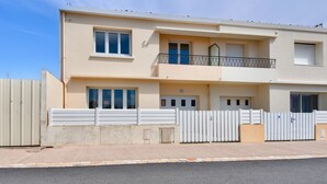A two-story residential building with a balcony, a gated entrance, and a clear sky. - 350m from the beach- House for 8- Large terrace (Saint-Hilaire-de-Riez)