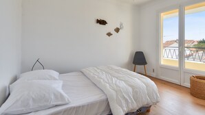A bedroom with a bed, a chair, and a window with a view of buildings. - 350m from the beach- House for 8- Large terrace (Saint-Hilaire-de-Riez)