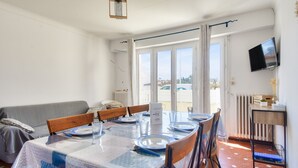 A dining area with a table set for four, a sofa, and a TV mounted on the wall. - 350m from the beach- House for 8- Large terrace (Saint-Hilaire-de-Riez)
