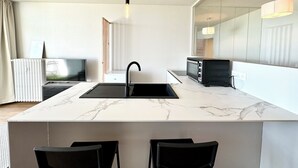 A modern kitchen with a marble countertop, a black sink, a microwave, and a black chair. - Appartement Top Cocooning – Vue mer 180° (Quiberon)