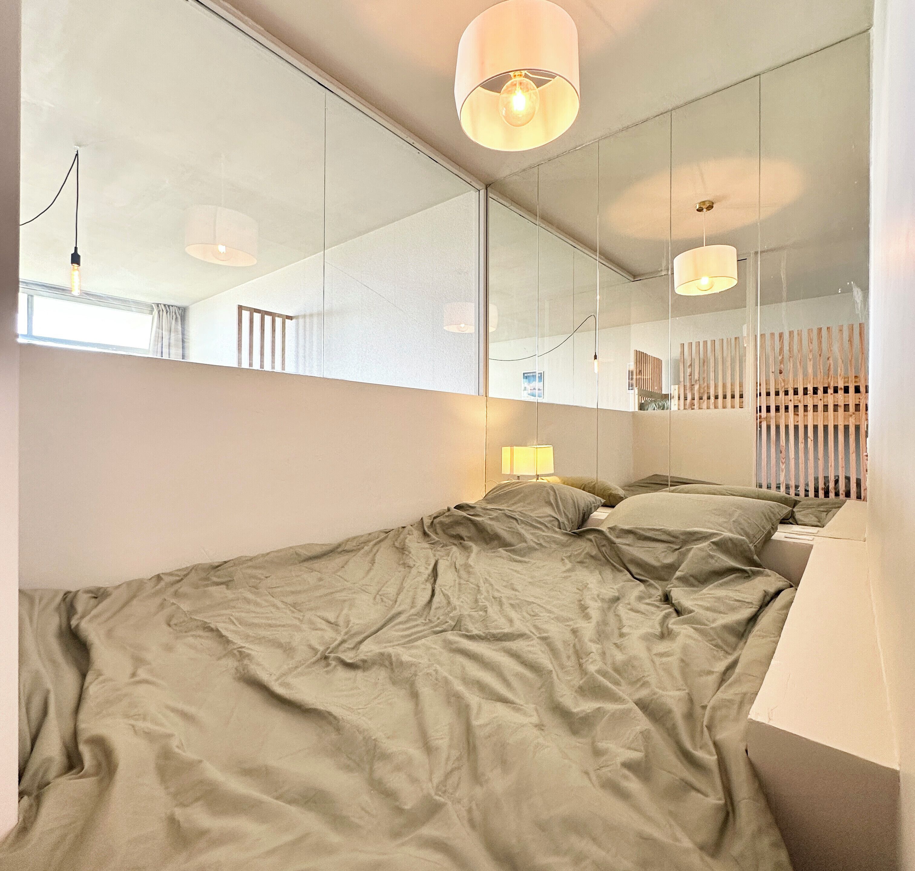 A modern bedroom with a large bed, a bedside lamp, and a mirror reflecting the room.