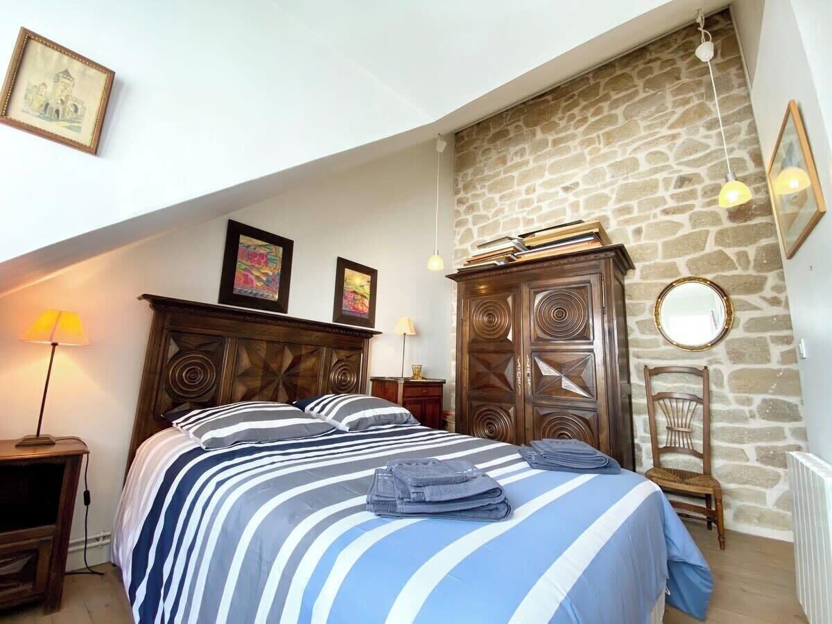 A bedroom with a bed, wooden wardrobe, stone wall, and a lamp.